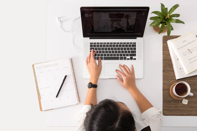 woman typing on laptop with notebook and coffee